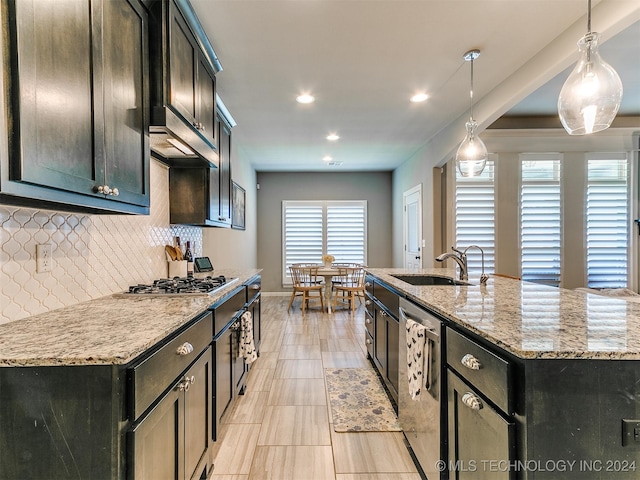 kitchen featuring appliances with stainless steel finishes, a kitchen island with sink, sink, pendant lighting, and light stone counters