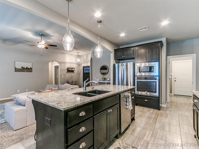 kitchen featuring an island with sink, appliances with stainless steel finishes, light stone countertops, sink, and decorative light fixtures