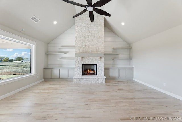 unfurnished living room featuring ceiling fan, light hardwood / wood-style floors, high vaulted ceiling, and a stone fireplace