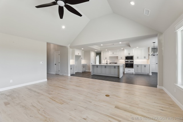 unfurnished living room with hardwood / wood-style floors, high vaulted ceiling, and ceiling fan with notable chandelier