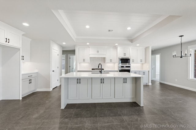 kitchen featuring a center island with sink, appliances with stainless steel finishes, a tray ceiling, and white cabinetry