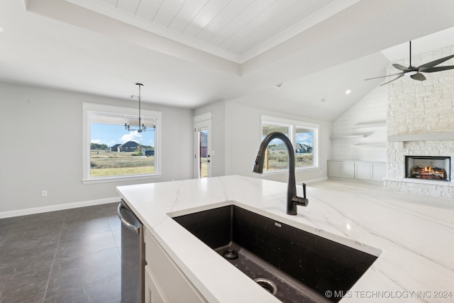 kitchen featuring lofted ceiling, dishwasher, hanging light fixtures, sink, and light stone counters