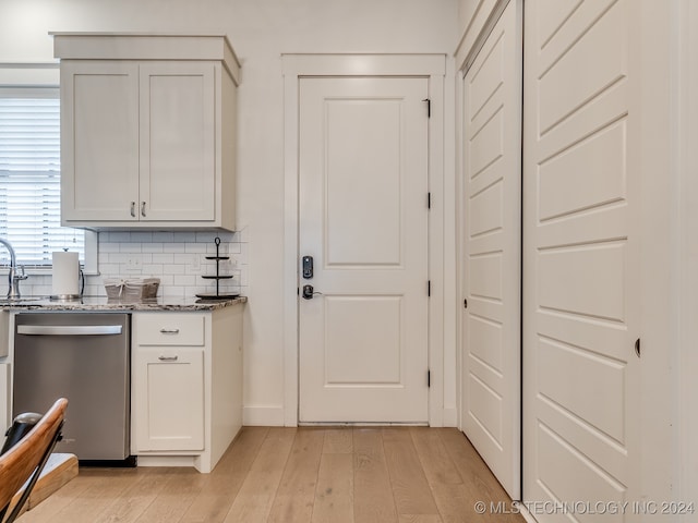 bar with dark stone countertops, tasteful backsplash, stainless steel dishwasher, and light wood-type flooring