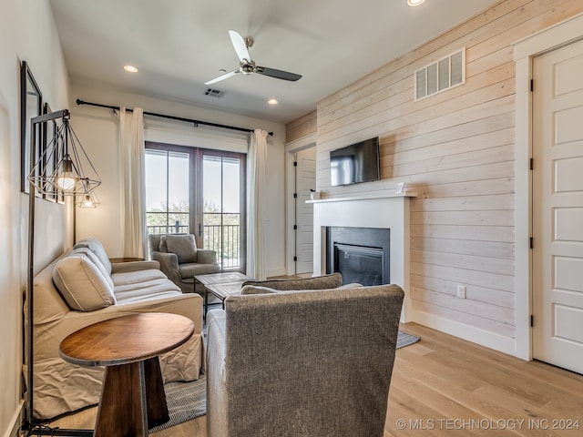 living room with light wood-type flooring, wood walls, and ceiling fan