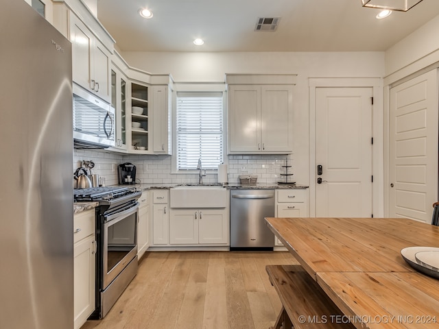 kitchen featuring stainless steel appliances, sink, white cabinetry, light hardwood / wood-style flooring, and dark stone countertops