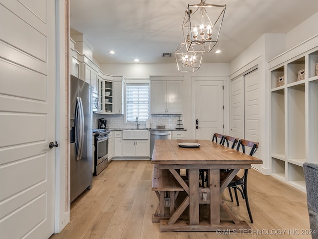 kitchen featuring light hardwood / wood-style flooring, hanging light fixtures, sink, white cabinetry, and appliances with stainless steel finishes