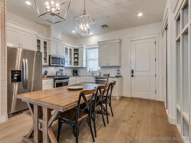 kitchen featuring stainless steel appliances, white cabinetry, light hardwood / wood-style flooring, and decorative light fixtures