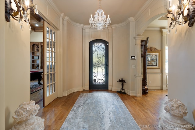 entryway with light hardwood / wood-style floors, crown molding, decorative columns, and an inviting chandelier