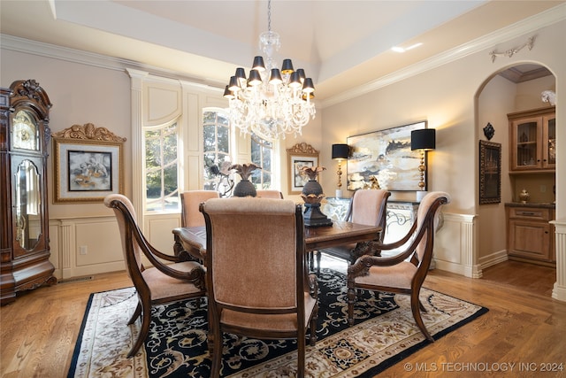 dining space featuring an inviting chandelier, ornamental molding, light wood-type flooring, and a raised ceiling