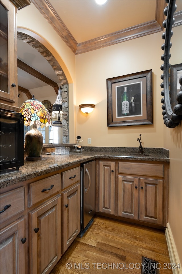 kitchen featuring wood-type flooring, sink, dark stone countertops, ornamental molding, and stainless steel refrigerator