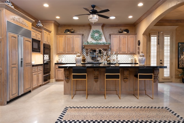 kitchen with ornamental molding, black appliances, an island with sink, and a kitchen bar