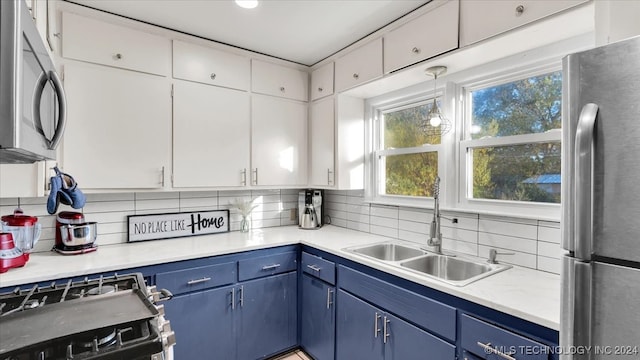 kitchen featuring stainless steel appliances, backsplash, sink, blue cabinetry, and white cabinets