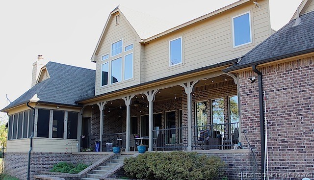 back of property featuring a sunroom, stairs, a chimney, and brick siding