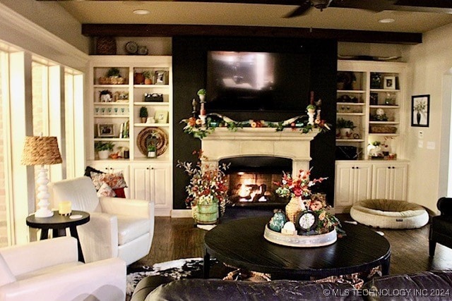 living room featuring a warm lit fireplace, wood finished floors, and built in features