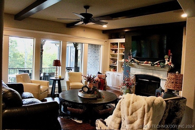 living area with a ceiling fan, beam ceiling, a fireplace, and wood finished floors