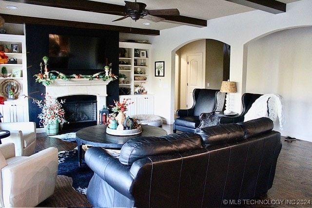 living area with wood finished floors, arched walkways, beamed ceiling, and a glass covered fireplace