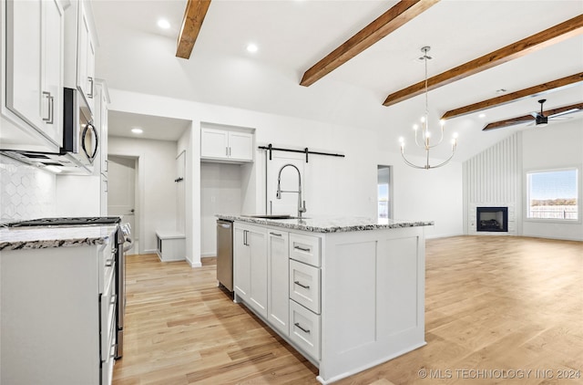 kitchen with white cabinets, hanging light fixtures, an island with sink, a barn door, and sink