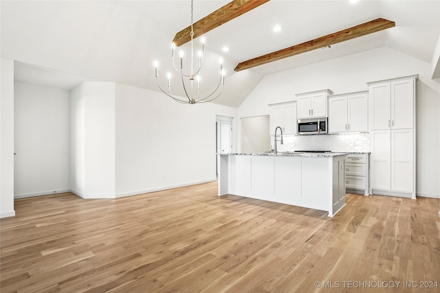 kitchen featuring an island with sink, lofted ceiling with beams, light stone counters, decorative backsplash, and light hardwood / wood-style flooring