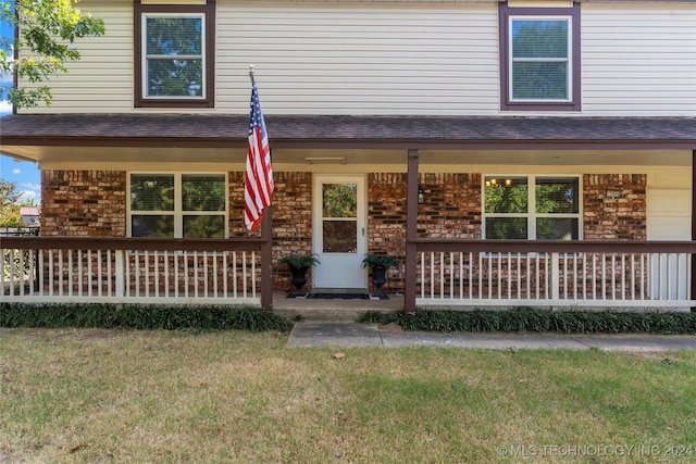 view of front of house featuring covered porch, roof with shingles, a front lawn, and brick siding