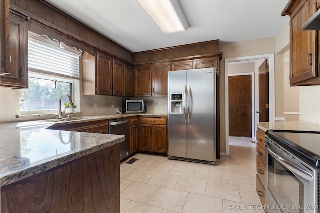 kitchen featuring tasteful backsplash, appliances with stainless steel finishes, light stone counters, wall chimney range hood, and a sink