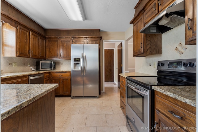 kitchen with light tile patterned floors, tasteful backsplash, light stone counters, stainless steel appliances, and under cabinet range hood