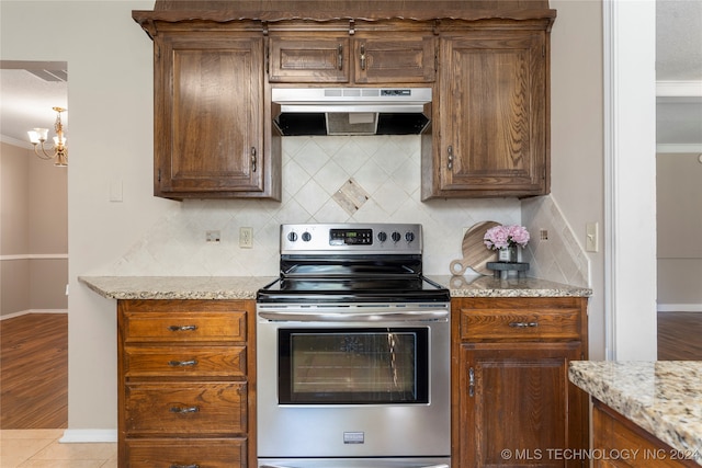 kitchen with light stone countertops, under cabinet range hood, stainless steel electric range, and backsplash