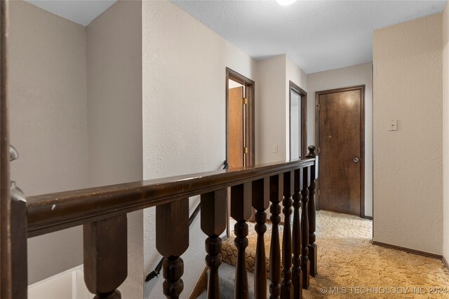 hall with a textured wall, baseboards, and light colored carpet