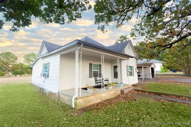 back house at dusk featuring a lawn and a porch