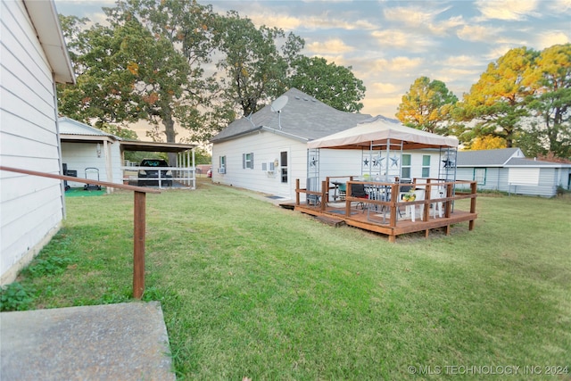 back house at dusk with a wooden deck and a lawn