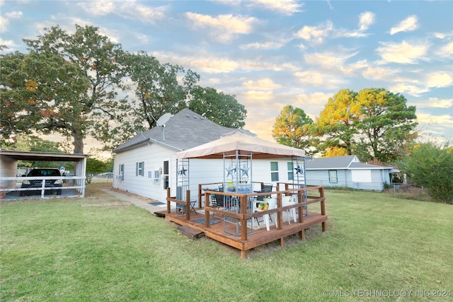 back house at dusk with a yard, a deck, and a carport