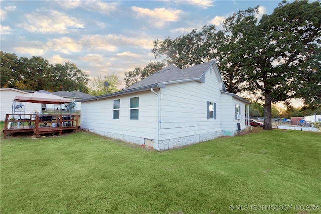 property exterior at dusk featuring a deck and a lawn