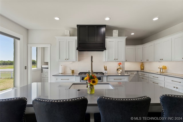 kitchen with a breakfast bar, white cabinetry, custom range hood, and backsplash