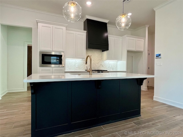 kitchen with light hardwood / wood-style floors, white cabinetry, stainless steel microwave, and an island with sink