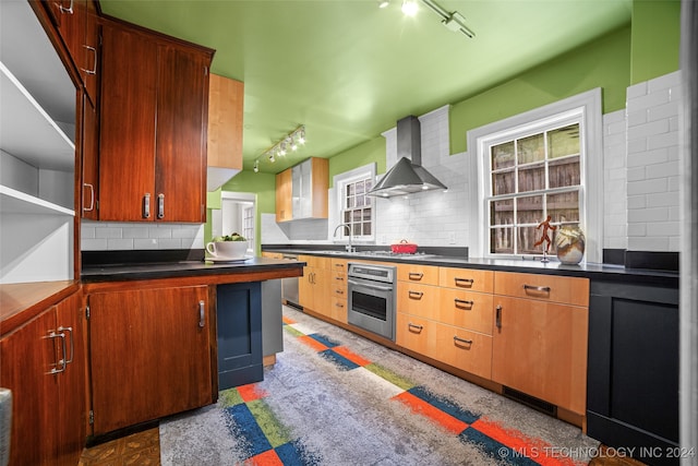 kitchen featuring wall chimney exhaust hood, stainless steel appliances, track lighting, and sink