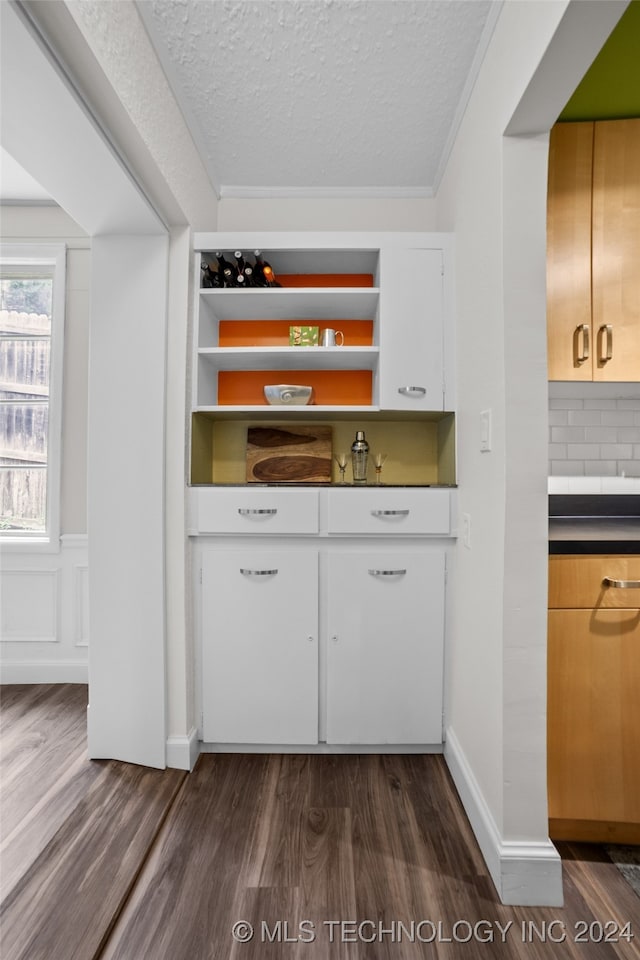 interior space featuring tasteful backsplash, a textured ceiling, white cabinetry, dark wood-type flooring, and ornamental molding