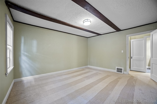 spare room with light carpet, a textured ceiling, and beamed ceiling