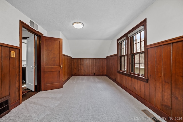 bonus room featuring lofted ceiling, wood walls, a textured ceiling, and carpet