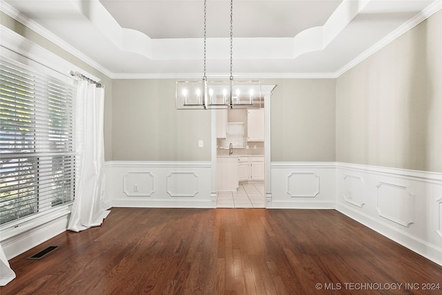 unfurnished dining area with a notable chandelier, hardwood / wood-style flooring, a tray ceiling, and crown molding