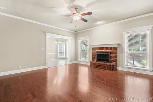 unfurnished living room featuring crown molding, hardwood / wood-style floors, ceiling fan with notable chandelier, and a brick fireplace