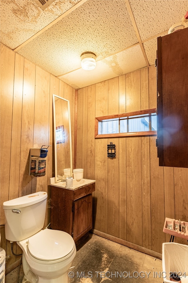 bathroom with toilet, a drop ceiling, and wooden walls