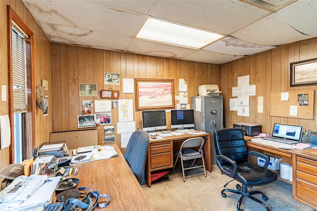 carpeted home office with a paneled ceiling and wooden walls