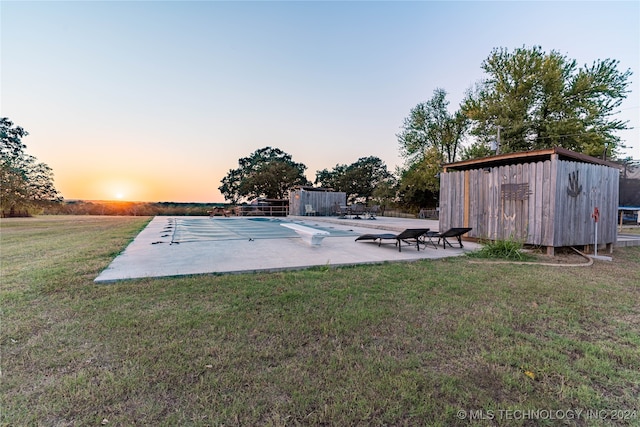 pool at dusk with a patio, a storage shed, and a lawn