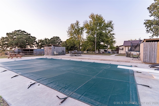 pool at dusk with a patio area and a diving board