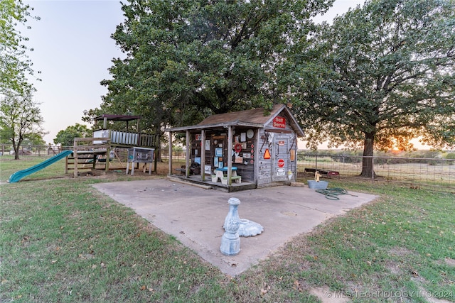 patio terrace at dusk with a playground, a yard, and an outbuilding