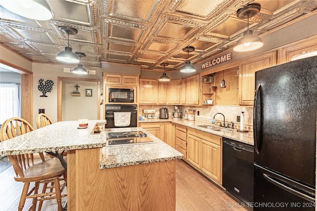 kitchen with black appliances, light stone counters, decorative light fixtures, and light wood-type flooring