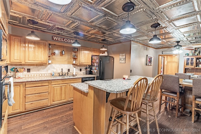 kitchen featuring dark wood-type flooring, hanging light fixtures, sink, black appliances, and light stone counters