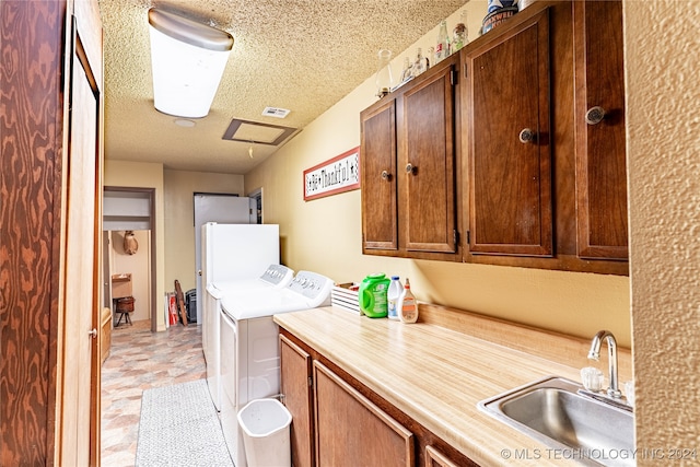 laundry area featuring sink, washing machine and dryer, a textured ceiling, and cabinets