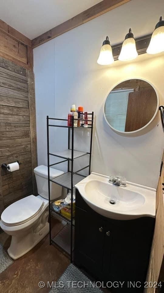 bathroom featuring toilet, vanity, concrete flooring, and wooden walls