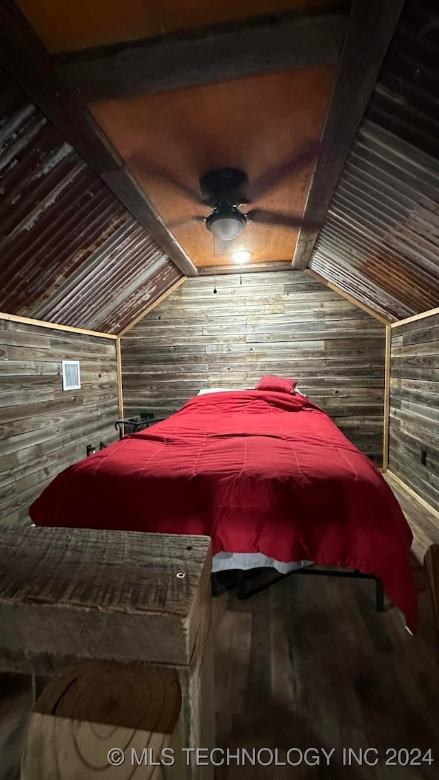 bedroom featuring ceiling fan, wood walls, lofted ceiling with beams, and hardwood / wood-style floors