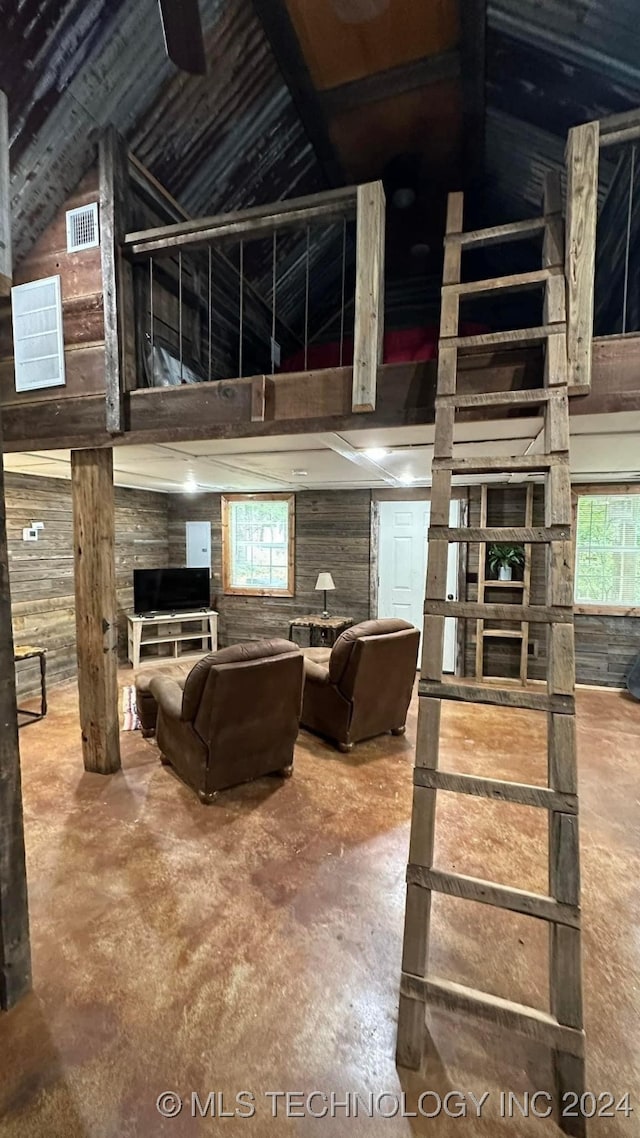 living room featuring high vaulted ceiling, a healthy amount of sunlight, wood walls, and concrete flooring